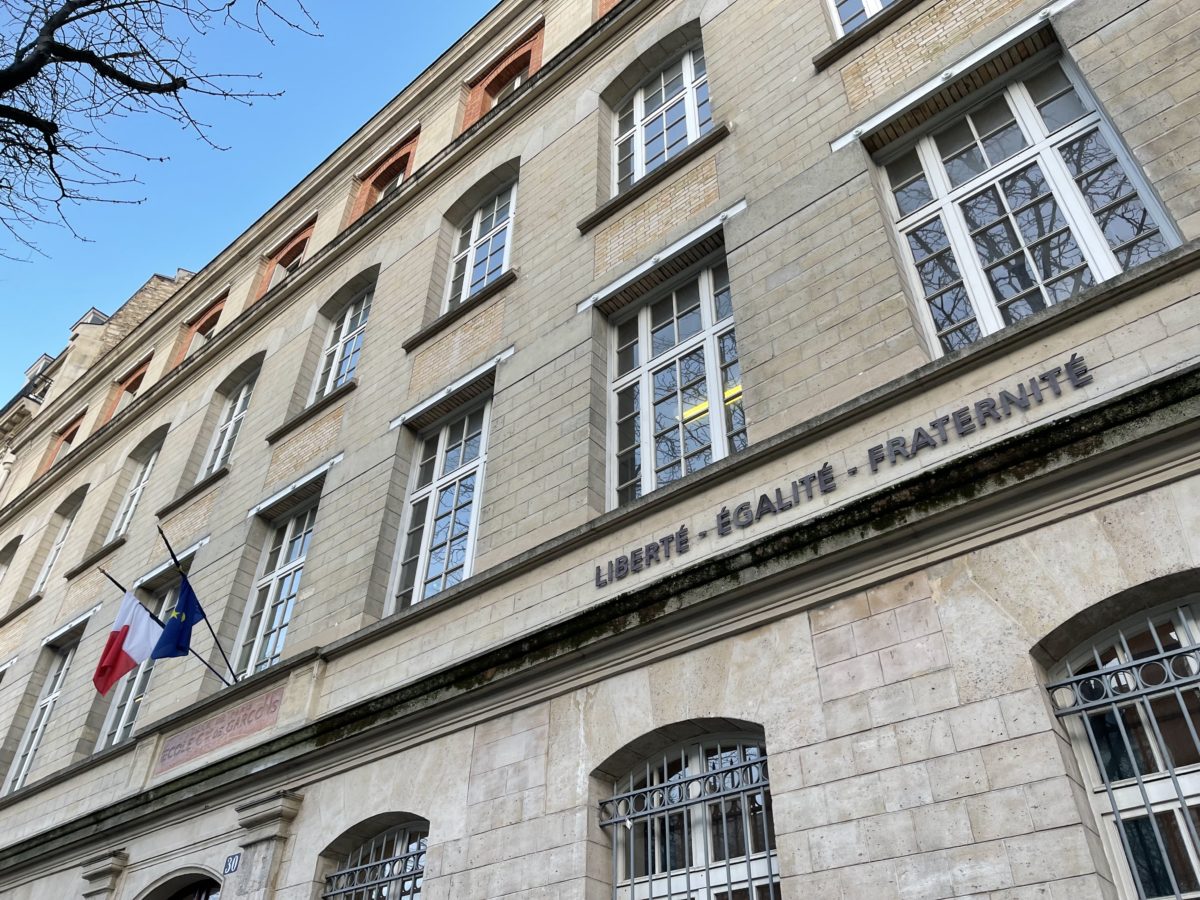 Vue partielle sur le fronton d'une école, le drapeau français et le drapeau européen sont accrochés et la devise Liberté, égalité, fraternité est inscrite.