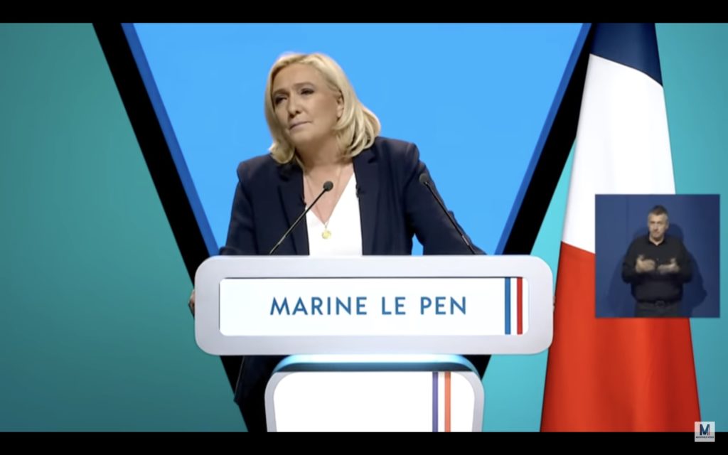 Capture d'écran : Marine Le Pen intervient en meeting, un médaillon LSF est visible sur le côté droit au milieu.