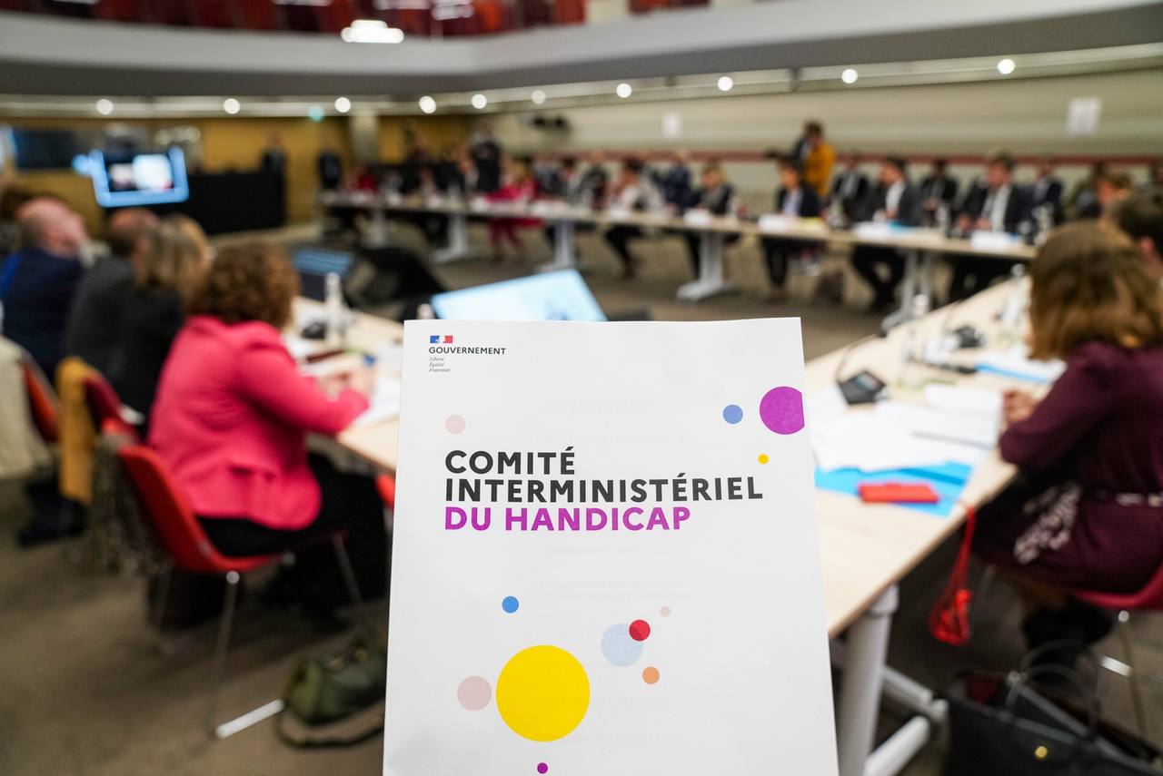 Couverture d'un dossier de presse sur le comité interministériel du handicap avec en arrière-plan les participants d'une réunion du comité assis autour d'une table.